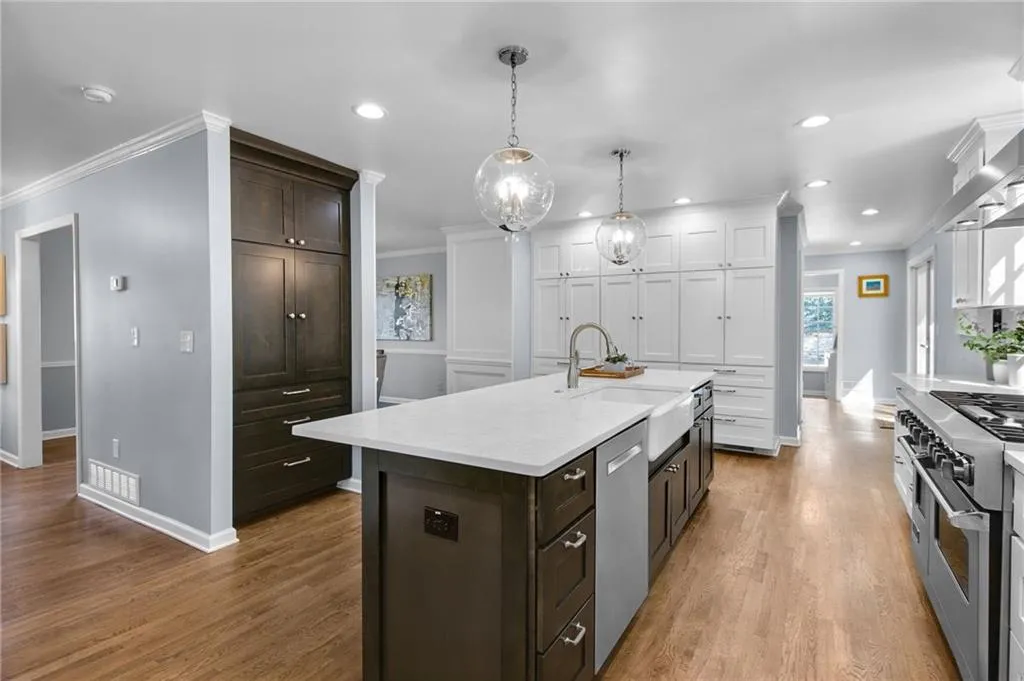 Kitchen with sink, decorative light fixtures, light hardwood / wood-style flooring, appliances with stainless steel finishes, and a kitchen island with sink