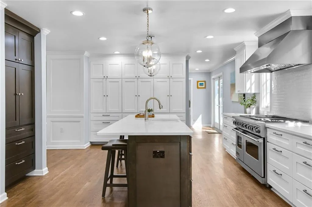 Kitchen with extractor fan, sink, white cabinets, double oven range, and a center island with sink