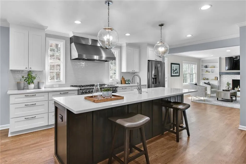 Kitchen featuring decorative light fixtures, an island with sink, white cabinets, stainless steel fridge with ice dispenser, and wall chimney exhaust hood