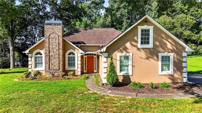Stucco exterior with a prominent brick chimney, arched windows, and a vibrant orange entry door