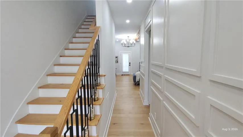 Hardwood flooring, painted wainscoting, a staircase with wood treads and a black metal baluster, and recessed lighting