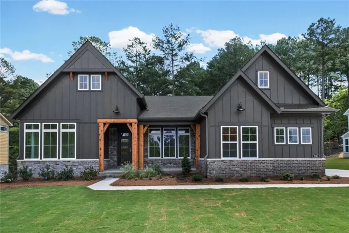 Charcoal board-and-batten siding with white trim, stone veneer foundation, natural wood porch columns, and a gabled roofline