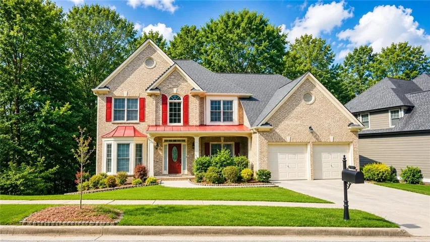 Traditional brick-front home featuring a two-car garage, red shutters, and a covered front porch