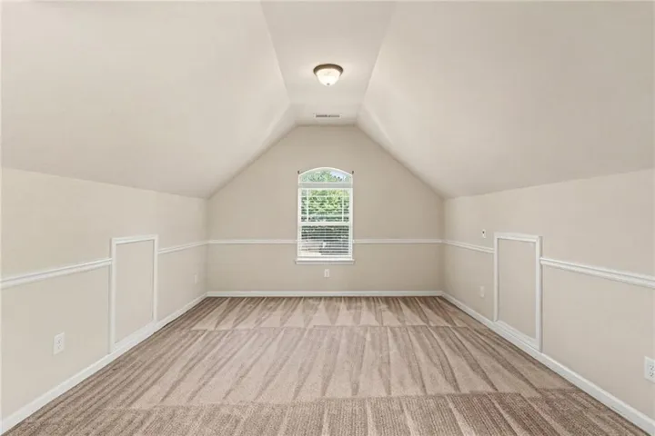 Arched window with blinds, vaulted ceiling, neutral wall color, carpet flooring, and integrated storage access
