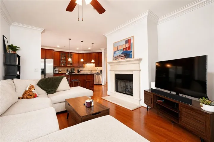 Living area with wood-finish flooring, a fireplace featuring a stone mantel, and crown molding