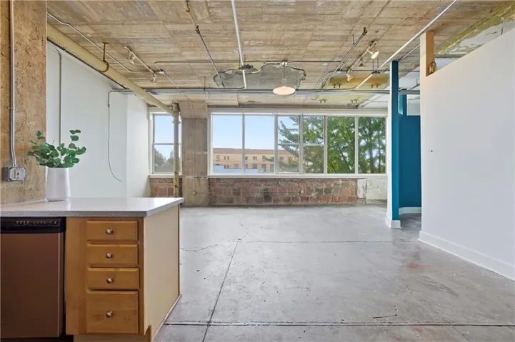 Kitchen with stainless steel dishwasher, unfinished concrete flooring, and light stone countertops