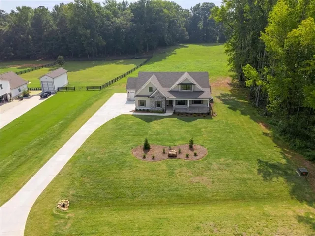 Expansive green lawn, mature trees surrounding the property, stone and siding exterior, covered front porch, and an attached garage