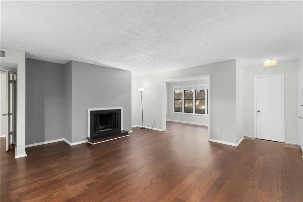 Unfurnished living room featuring a fireplace with raised hearth, dark wood finished floors, and a textured ceiling