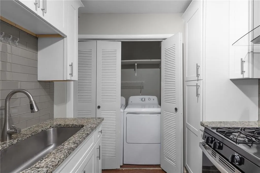 Kitchen with white cabinetry, washer and dryer, range with gas stovetop, and light stone countertops