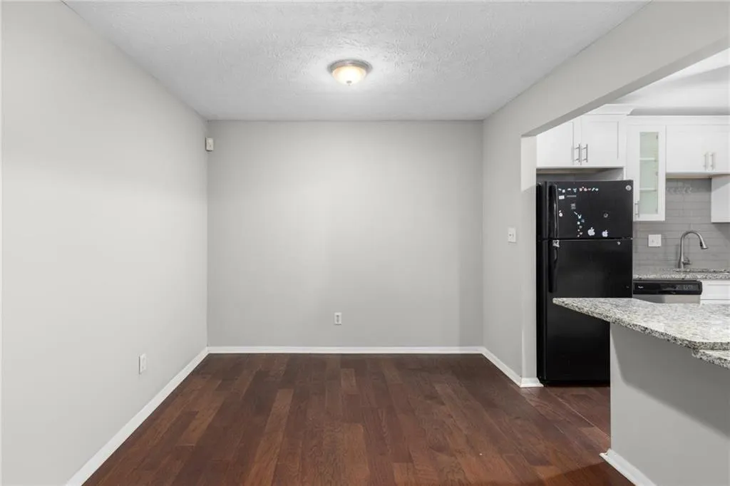 Kitchen with freestanding refrigerator, a textured ceiling, backsplash, dark wood-style flooring, and light stone counters