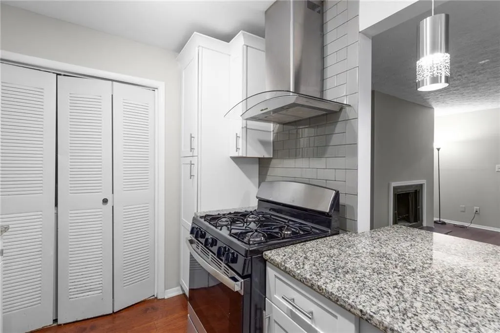 Kitchen with gas stove, dark wood-style floors, wall chimney exhaust hood, light stone counters, and decorative backsplash