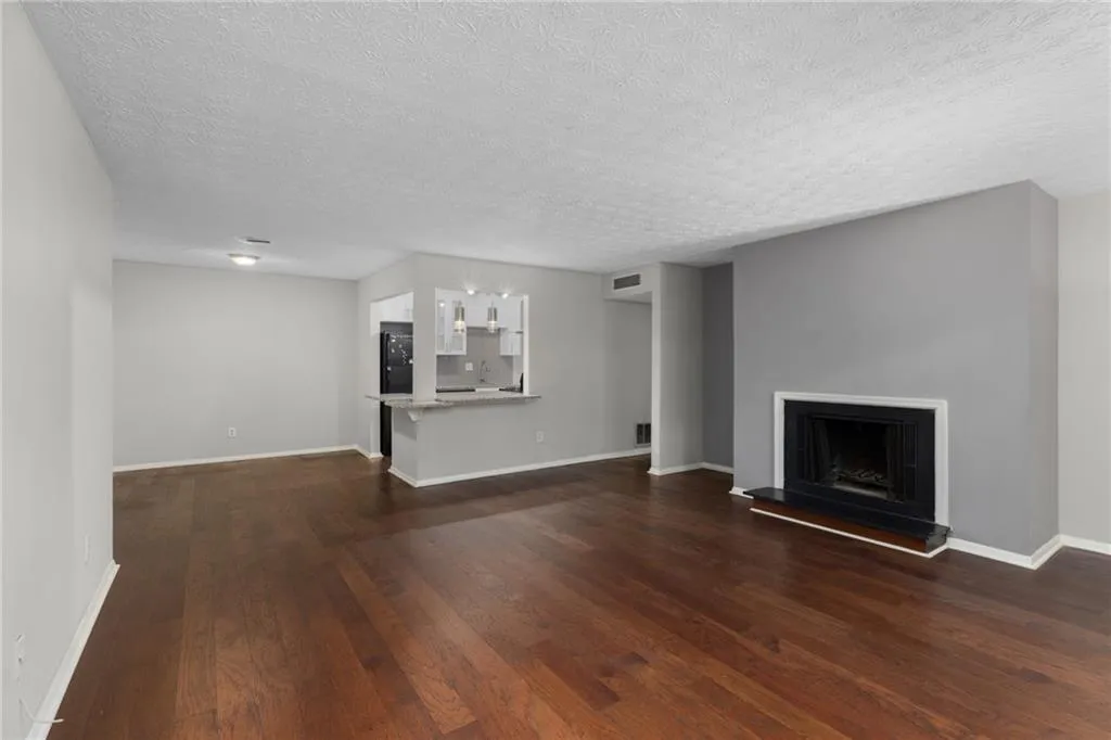 Unfurnished living room with a fireplace with raised hearth, dark wood-type flooring, and a textured ceiling