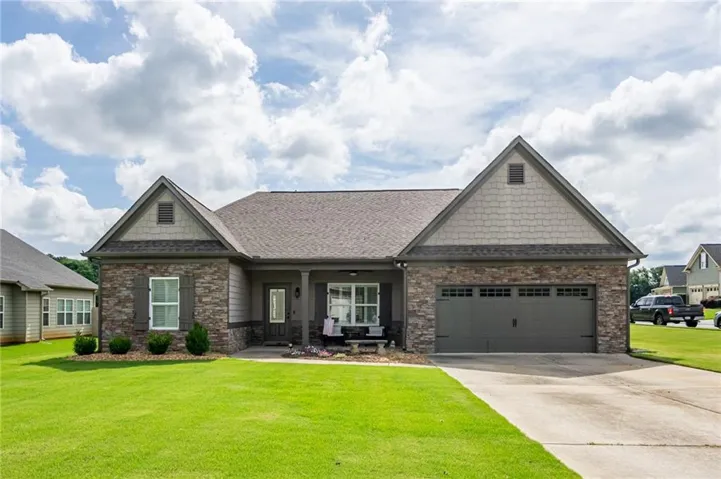 Single-story residence featuring a stone and siding facade, a two-car garage with a concrete driveway, a covered front porch, and a shingle roof