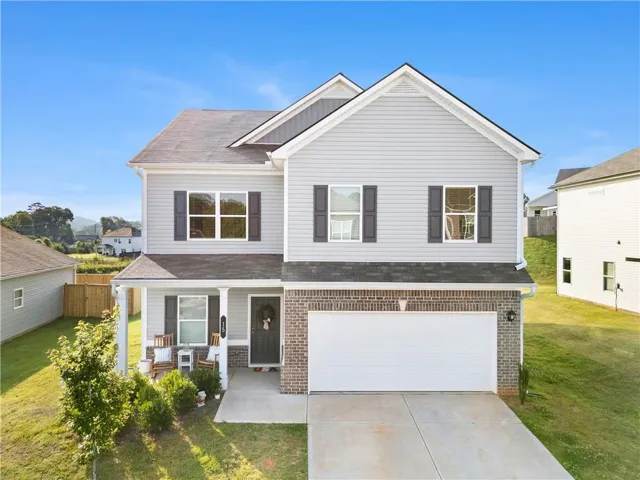 Two-story residence featuring light gray siding with dark shutters, a front porch with white columns, and a two-car garage with a concrete driveway