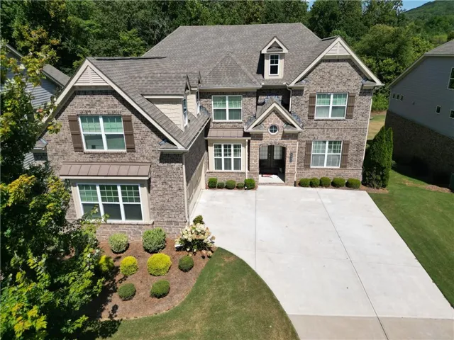 Brick facade with stone accents, multiple gables, a dormer, a concrete driveway, and established front landscaping