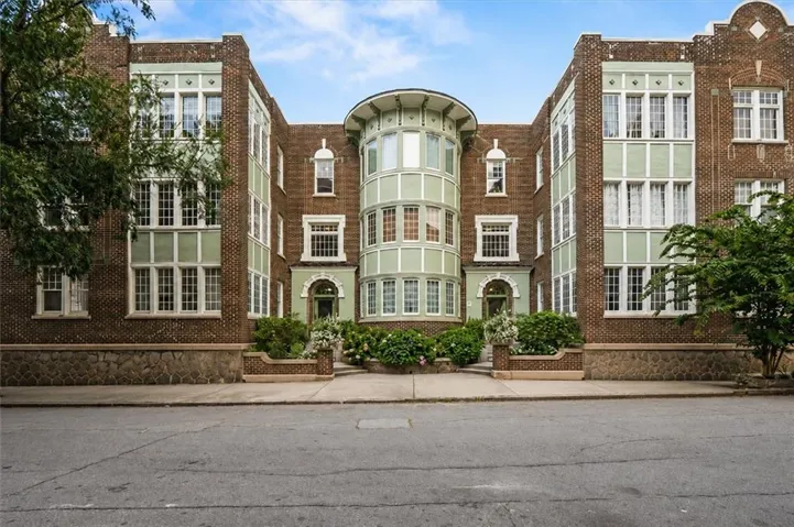 Brick exterior featuring a central curved bay window, light green trim, stone foundation, and multiple arched entryways