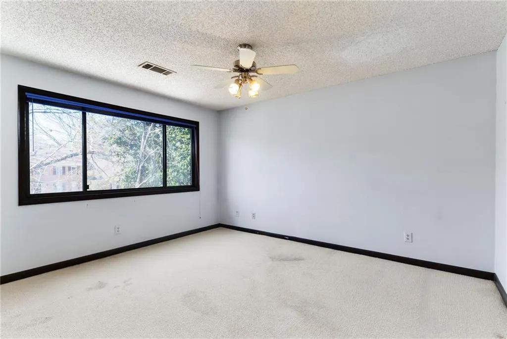 Carpeted spare room featuring a ceiling fan, baseboards, visible vents, and a textured ceiling