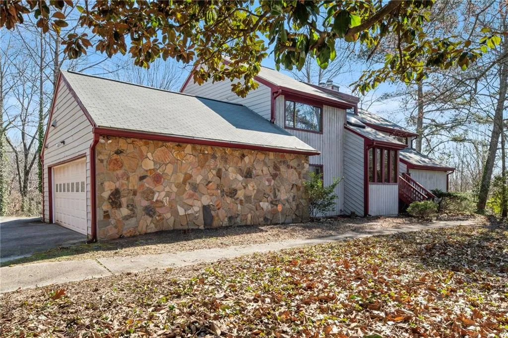 View of side of home featuring a shingled roof, stone siding, driveway, and a chimney