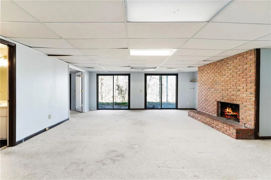 Unfurnished living room featuring a paneled ceiling, a brick fireplace, baseboards, and carpet
