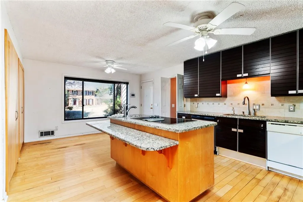 Kitchen with black electric stovetop, a sink, light wood-type flooring, dishwasher, and an island with sink