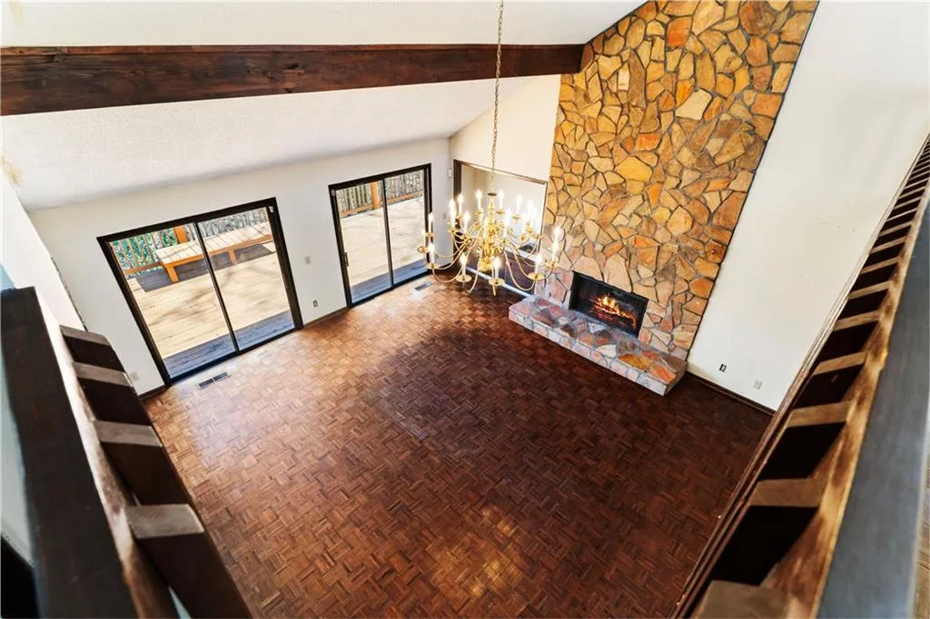 Unfurnished living room featuring a notable chandelier, visible vents, a stone fireplace, high vaulted ceiling, and beamed ceiling