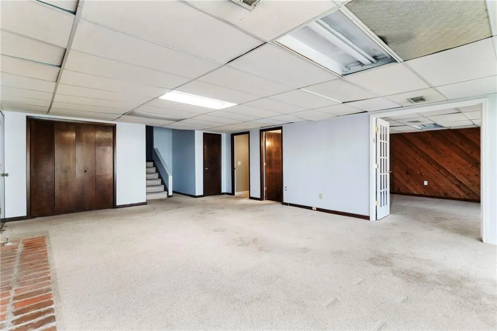 Finished basement with a drop ceiling, wooden walls, carpet floors, baseboards, and stairs