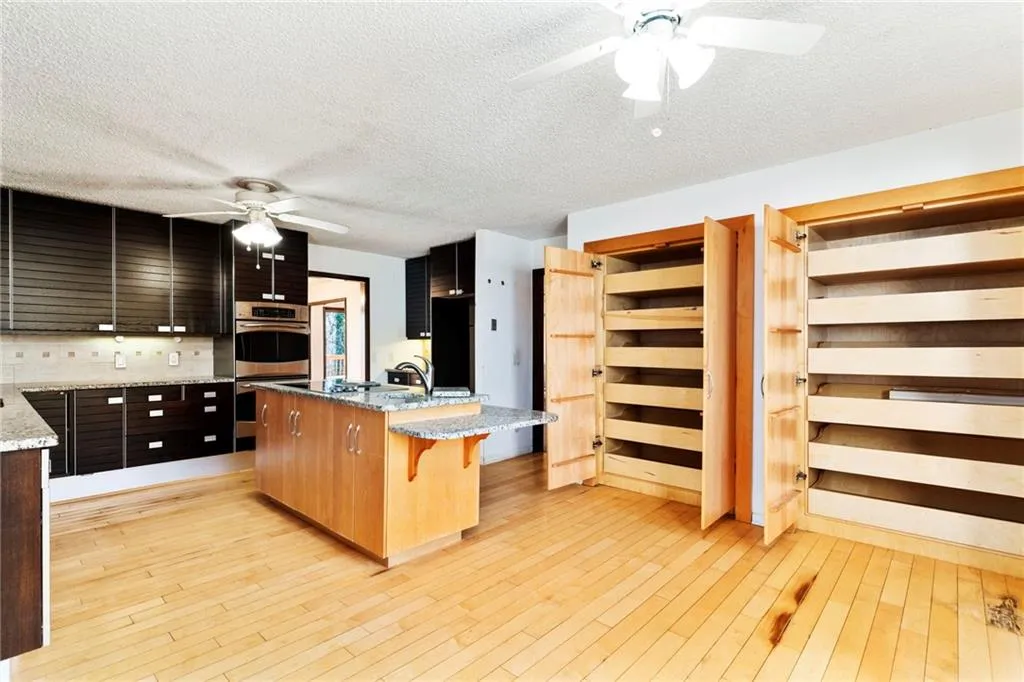 Kitchen with light wood finished floors, an island with sink, ceiling fan, a breakfast bar area, and light stone countertops