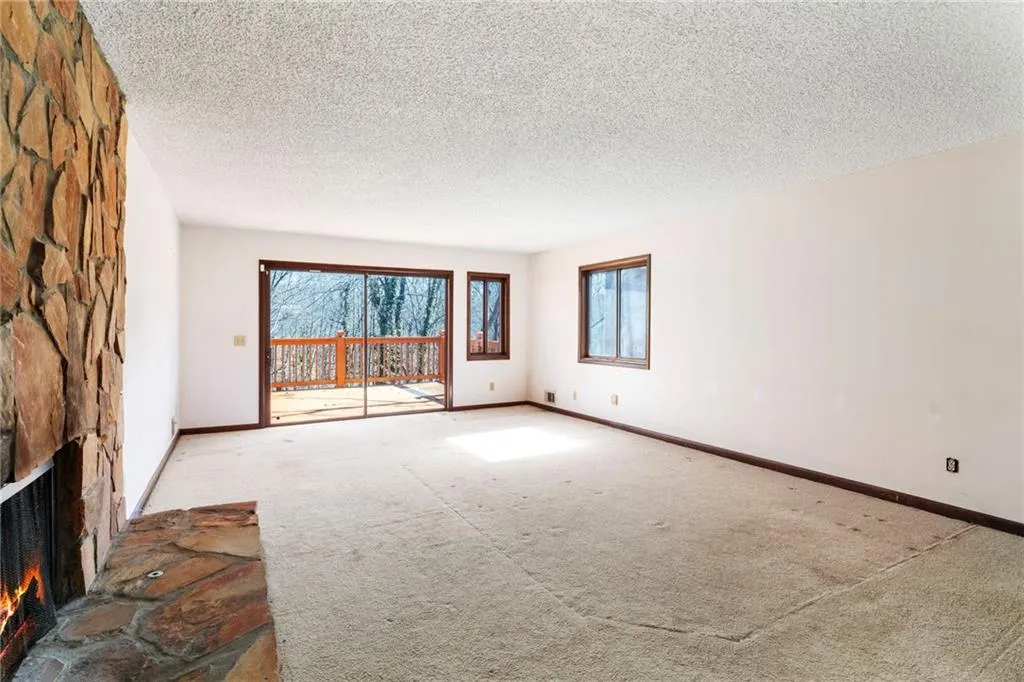 Spare room with carpet, a stone fireplace, and baseboards