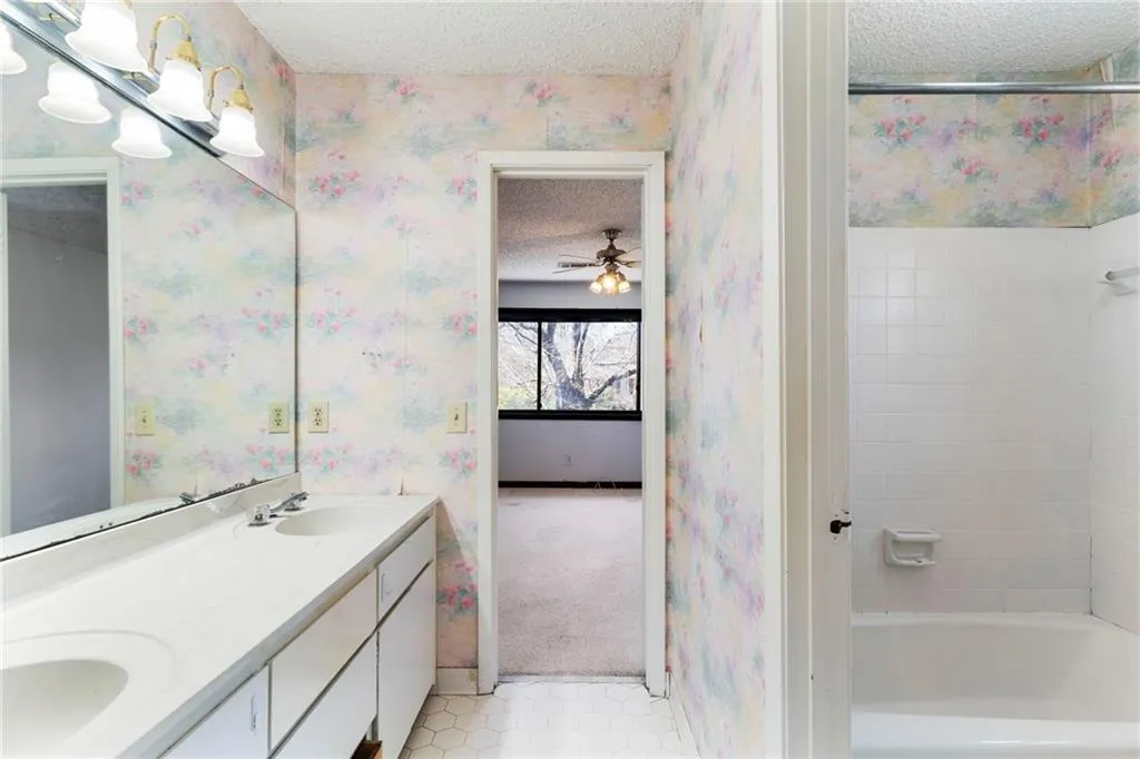 Full bath featuring double vanity, a ceiling fan, a sink, a textured ceiling, and wallpapered walls