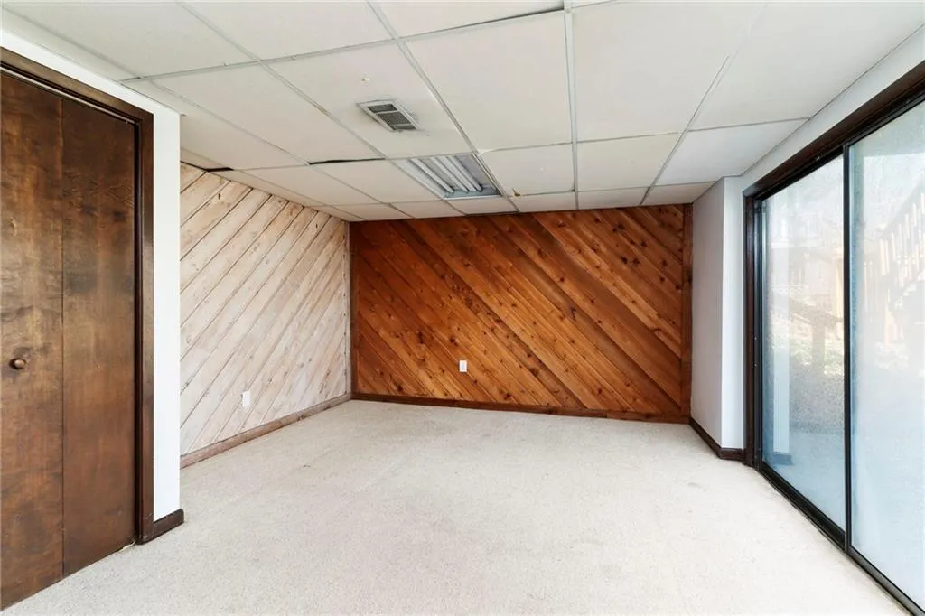 Spare room with wooden walls, visible vents, a drop ceiling, and light colored carpet