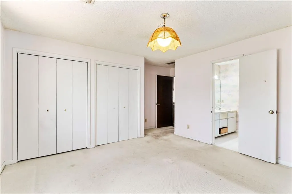 Unfurnished bedroom with a textured ceiling, ensuite bath, two closets, and baseboards