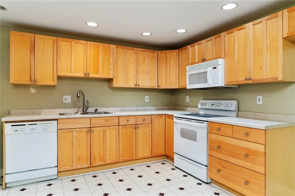 Kitchen featuring white appliances, light countertops, light brown cabinetry, a sink, and recessed lighting