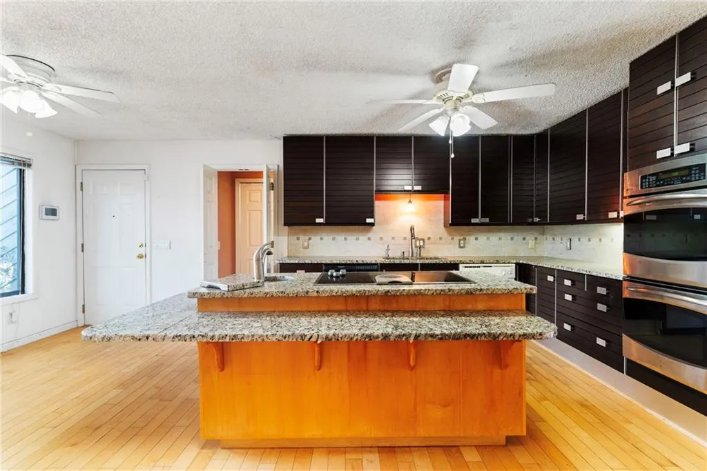 Kitchen with a breakfast bar area, stainless steel double oven, black electric cooktop, a sink, and light wood-style floors
