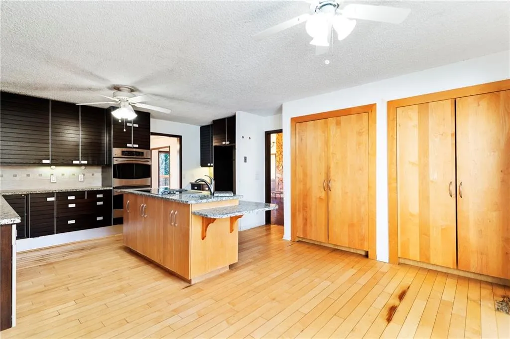 Kitchen with an island with sink, ceiling fan, a breakfast bar, stainless steel double oven, and light wood-type flooring