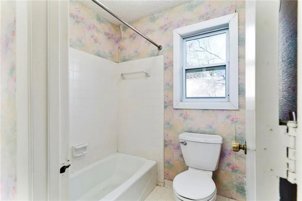 Bathroom featuring wallpapered walls, baseboards, toilet,  shower combination, and a textured ceiling
