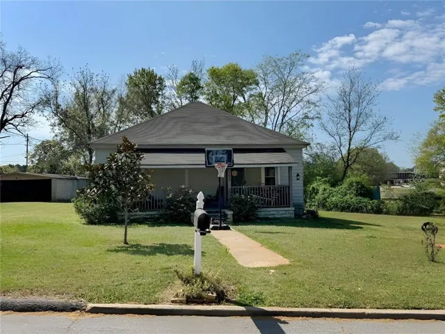 Single-story residence featuring a covered front porch with vertical column supports, a paved walkway, a dark asphalt shingle roof, and a mature tree in the front yard