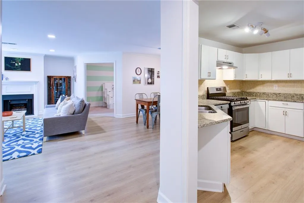 Kitchen featuring stainless steel range with gas stovetop, under cabinet range hood, light stone counters, backsplash, and light wood-style flooring