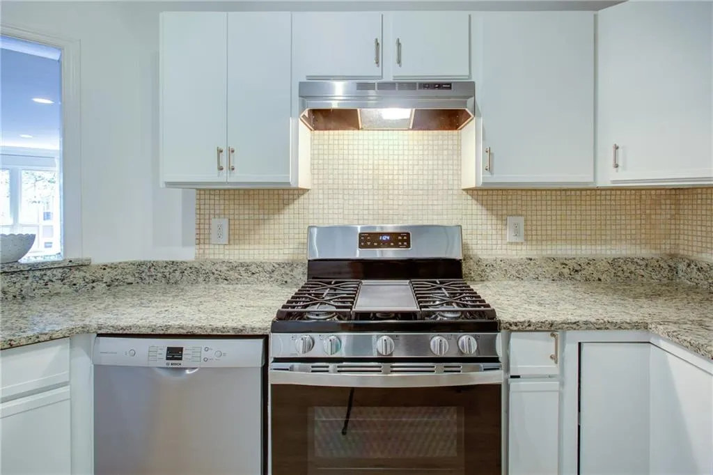 Kitchen featuring stainless steel gas range, under cabinet range hood, dishwasher, and white cabinets
