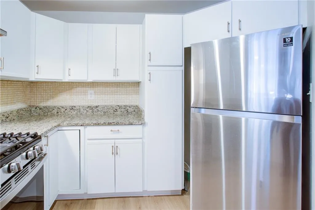 Kitchen with appliances with stainless steel finishes, light stone counters, white cabinetry, decorative backsplash, and light wood finished floors