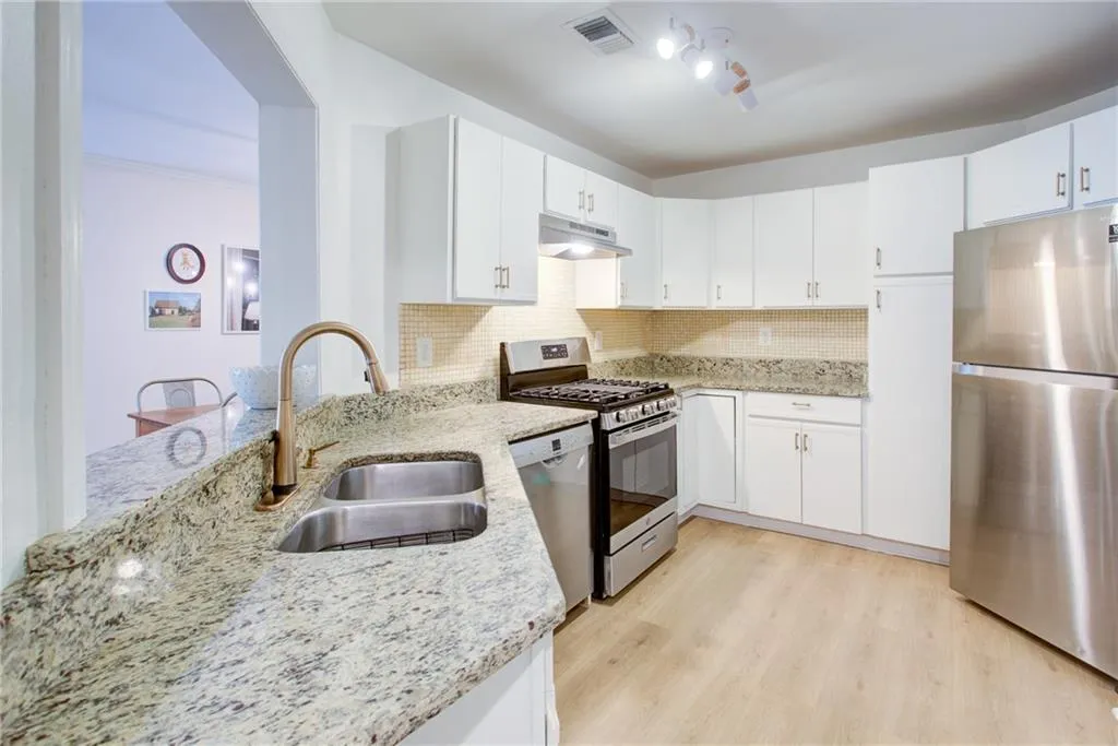Kitchen with stainless steel appliances, under cabinet range hood, light stone counters, tasteful backsplash, and crown molding