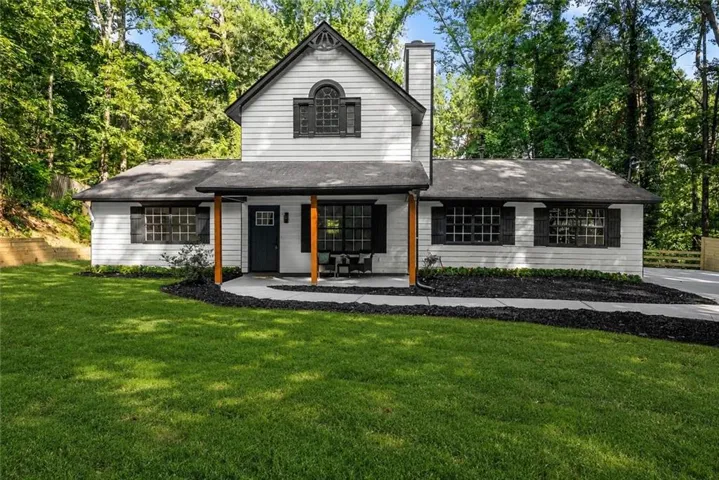 White siding exterior with black shutters, a covered porch with natural wood columns, and a large lawn