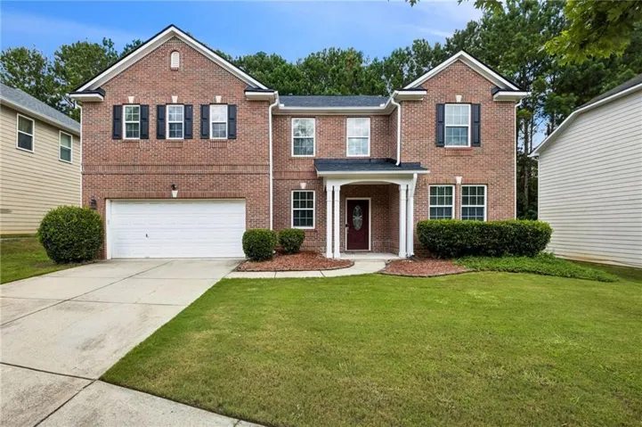 Traditional brick two-story residence featuring a two-car garage, a covered front entry, and black louvered shutters