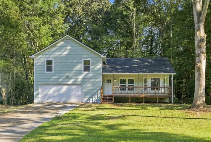 Light green siding exterior with a dark shingle roof, featuring a covered porch with white railings and a two-car garage with a white door