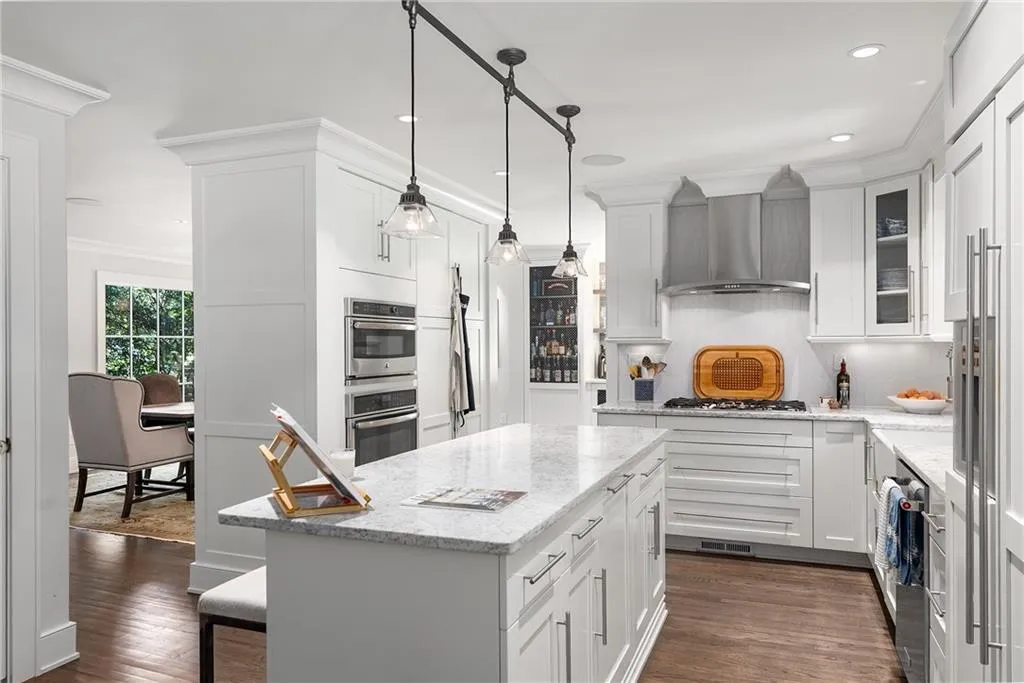 Kitchen featuring light stone counters, ornamental molding, a kitchen island, dark wood-style floors, and hanging light fixtures