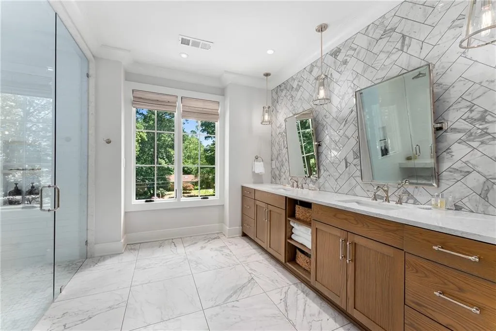 Bathroom featuring crown molding, double vanity, a shower stall, backsplash, and light marble finish flooring