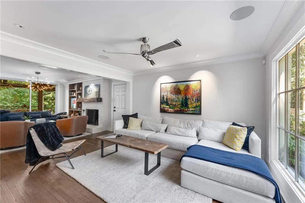 Den area with crown molding, a fireplace, wood finished floors, and a ceiling fan