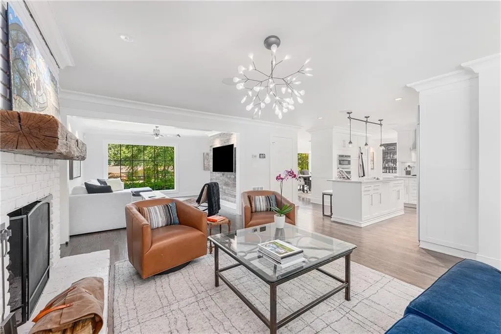 Living room with a brick fireplace, light wood finished floors, crown molding, recessed lighting, and a chandelier