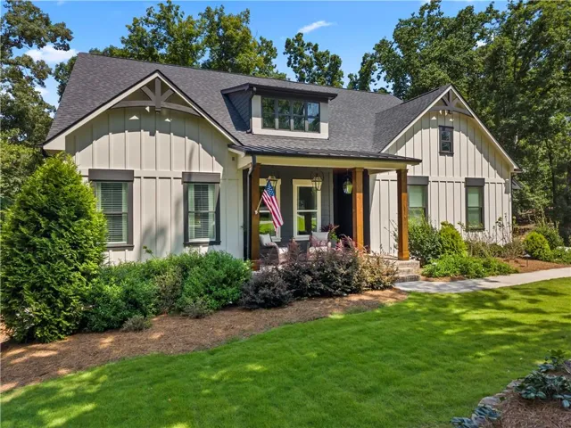 Craftsman-style exterior featuring board and batten siding, dark framed windows, a welcoming front porch with wood columns, a dark shingle roof, and established landscaping