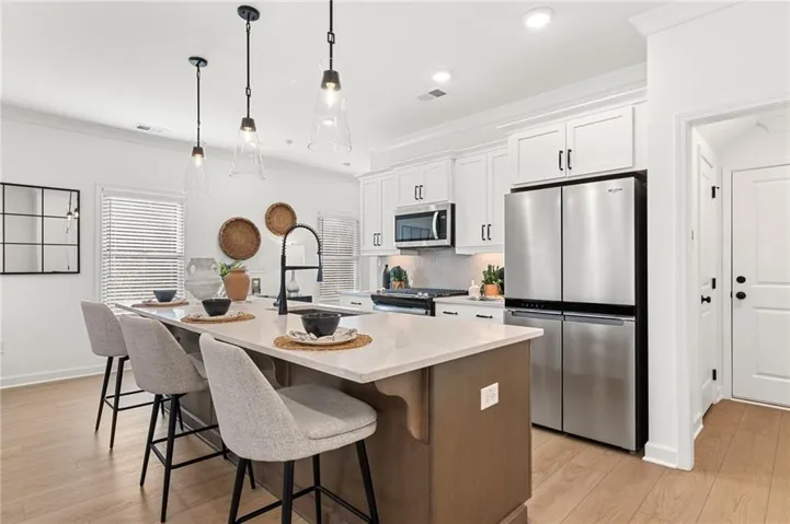 Modern kitchen featuring a central island with countertop seating, stainless steel appliances, white shaker cabinetry, and wood-finish flooring