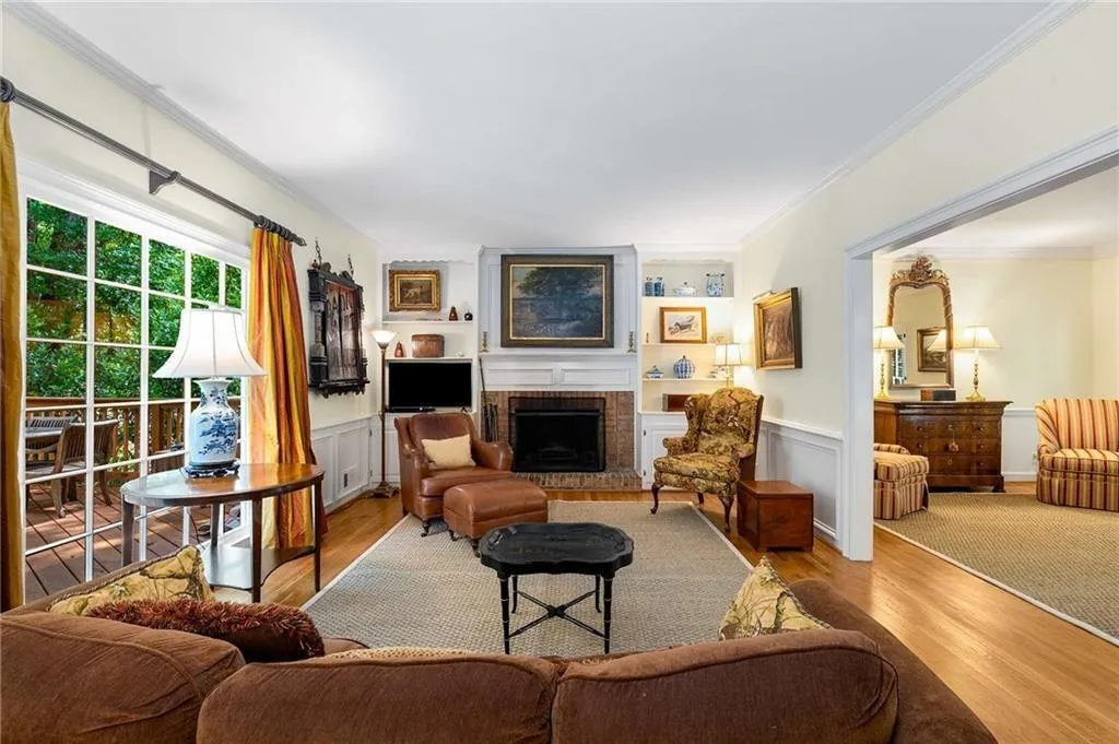 Den/family room featuring hardwood floors, ornamental molding, a brick fireplace, wainscoting and view to backyard and deck.